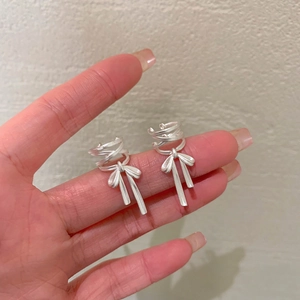 Silver bow ribbon ear bone clip with tassel drops for non-pierced ears on a hand