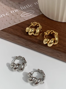 Detailed view of gold and silver twisted metallic hoop earrings on a wooden display