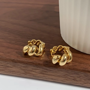 Polished 18K gold croissant hoop earrings with a twisted design on dark wood surface