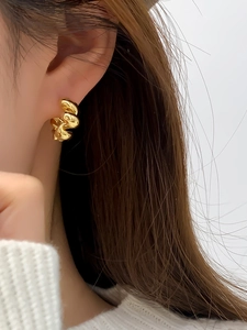 Close-up of golden spiral twist hoop earrings with a polished finish worn on a model