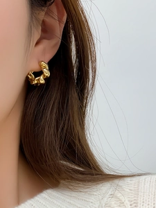 Close-up of elegant gold twisted hoop earring worn by a model in a minimalist style