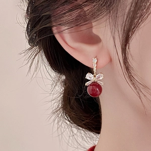 Close-up of elegant bow earrings with burgundy pearls and sparkling crystals on model