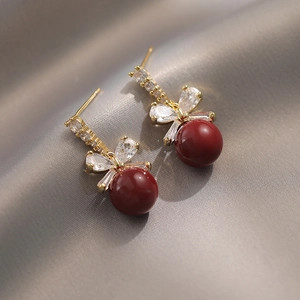 Close-up of golden bow earrings with sparkling crystals and deep red round pearl drop