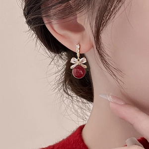 Detail of red pearl bow earrings with gold plating and zircons on a female model