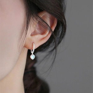 Elegant twisted silver hoops with heart-shaped moonstone pendants on a model side profile