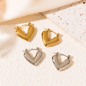 Macro shot of polished gold and silver heart earrings on a natural stone surface