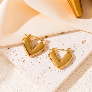 Detailed close-up of polished gold heart-shaped earrings on a textured stone surface