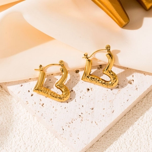 Detail of gold heart earrings with hammered texture on a white stone background