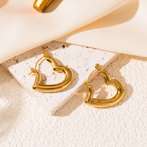 Polished gold heart earrings on a beige stone base with cream silk fabric background