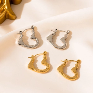 Detailed view of gold and silver heart hoop earrings with hammered texture on silk fabric