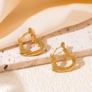 Detail of gold heart hoop earrings with hammered texture on a beige stone surface