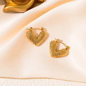 Close-up of golden heart-shaped earrings with textured surface on white silk