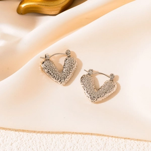 Macro detail of silver heart earrings with textured dot finish on silk background