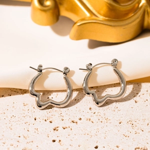Detailed close-up of silver irregular wave hoop earrings on a beige textured stone slab