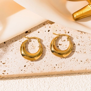 Close-up of chunky gold-plated stainless steel geometric hoop earrings on a stone slab