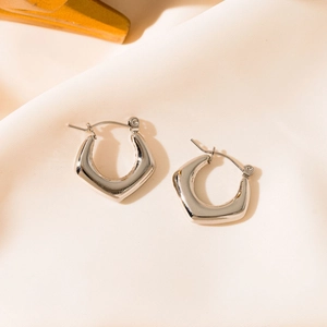 Macro view of geometric silver earrings with polished finish on beige fabric texture