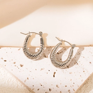 Detailed view of silver hoop earrings with twisted spiral texture on beige stone