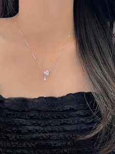 Detail of silver heart necklace with 'Love' charm and teardrop zircon on a model