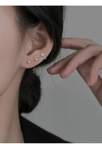Gros plan des clous d'oreilles nœud Ruyi et billes en argent portés sur le cartilage