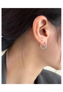 Détail de la créole torsadée argentée et du clou d'oreille rond en zircone cubique