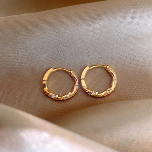 Élégantes créoles torsadées dorées avec zircons sur fond de satin de couleur champagne