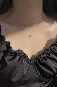 Détail du collier avec anneau en argent S925 sur une robe plissée noire sous la lumière