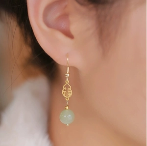 Detailed close-up of a hollow gold gourd earring with Fú character and green jade bead