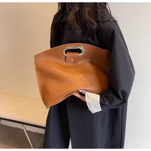 Detail of caramel brown oversized leather clutch with oval metal handle and soft texture