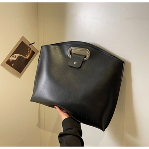 Close-up of black leather tote bag featuring a unique silver metal cutout handle