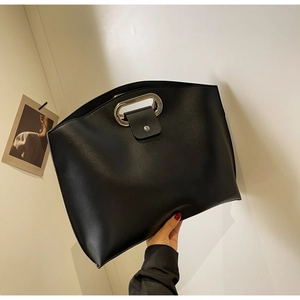 Detail of black leather tote bag featuring a silver oval metal handle and embossed logo
