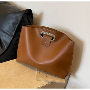 Detail of caramel brown leather handbag featuring silver oval metal handle and logo