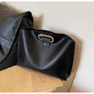 Detail of black matte leather tote bag with oval metal handle on stone surface