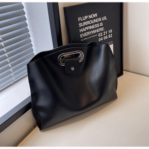 Detail of minimalist black leather tote bag with silver oval metal handle on white desk