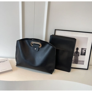 Detail of minimalist black leather tote bag with metal handle and magnetic clutch bag