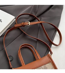 Detail of adjustable brown leather shoulder strap and buckle on a plaid pattern bag