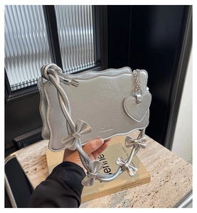 Detail of silver metallic shoulder bag with bow-knot strap and wavy edge design