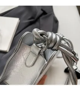 Detail of silver metallic textured bag featuring round hardware and unique knotted shoulder strap
