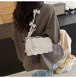 Detail of silver wavy shoulder bag with bow straps and heart pendant in lifestyle view