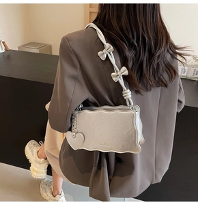Detail of silver metallic wavy shoulder bag with heart pendant and bow accents
