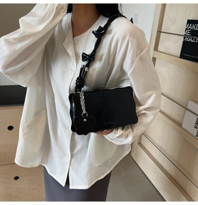 Black minimalist shoulder bag featuring wavy edges, bow strap, and a heart charm detail