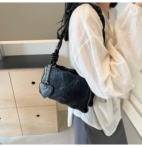 Detail of black glossy textured shoulder bag featuring wave edges and heart charm