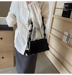Detail of black shoulder bag with wavy edges and heart charm worn by a model