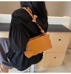 Detail of camel shoulder bag with scalloped edges and heart charm plus bow strap design