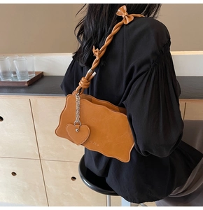 Detail of caramel shoulder bag with wave edges, bow strap, and heart charm accessory