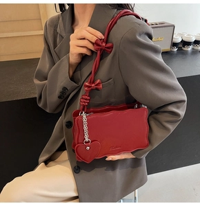 Detail of red wavy-edge shoulder bag featuring bow decorations and heart pendant
