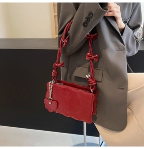 Detail of red shoulder bag with wavy edges and decorative bow strap with heart charm