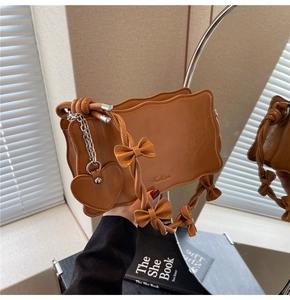 Detail of caramel leather handbag featuring wavy edges and bow-knotted handle with heart charm