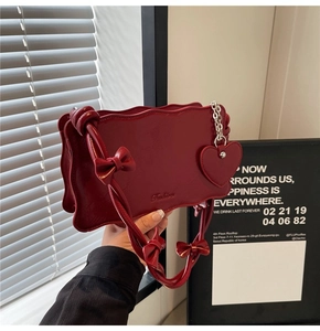 Detail of burgundy glossy leather handbag with wavy edges and heart-shaped charm