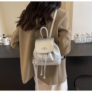 Detail of silver small backpack with litchi texture and drawstring flap closure on model