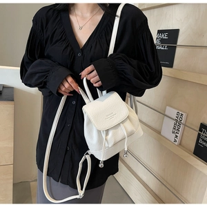 Close-up of white mini backpack with lychee leather texture and drawstring metal beads